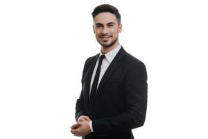 Young and successful. Handsome young man in full suit adjusting his sleeve and looking at camera while standing against white background photo