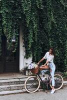 Enjoying nice day. Full length of attractive young woman in casual wear looking down while standing in front of the house covered with ivy photo