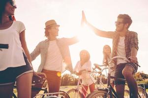 High five Low angle view of cheerful young people standing near their bicycles on the road while two men giving high five photo