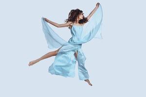 Feeling free to do anything. Full length studio shot of attractive young woman in elegant dress keeping arms outstretched while hovering against grey background photo