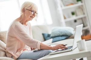 Interesting... Beautiful senior woman writing something down while sitting on the couch at home photo