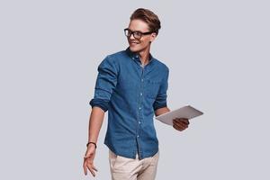 Confident student. Handsome young man looking away and smiling while standing against grey background photo