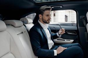 Confident businessman. Handsome young man in full suit looking away while sitting in the car photo