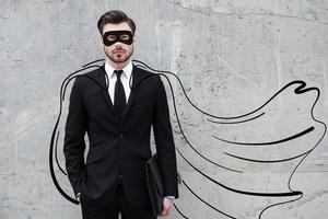 héroe en su negocio. un joven hombre de negocios confiado que lleva una capa y una máscara dibujadas mientras está de pie contra una pared de hormigón foto