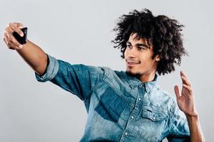 Selfie from handsome. Cheerful young African man making selfie while standing against grey background photo