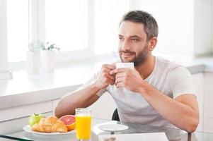 Comenzando el día con café recién hecho y caliente. un joven apuesto que disfruta de un café recién hecho mientras está sentado en la cocina foto