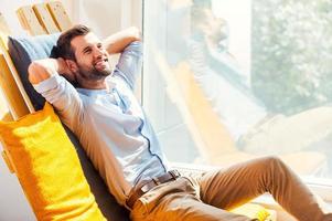 Total relaxation. Cheerful young man holding head in hands and smiling while sitting in the rest area of the office photo