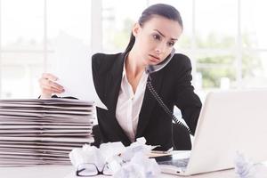 Busy working. Confident young woman in formalwear with documents and talking on the telephone while sitting at her working place photo