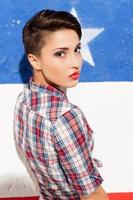 Cool beauty. Rear view of beautiful young short hair woman standing against American flag background and looking over shoulder photo