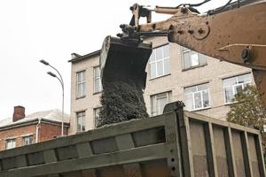 obras viales en la calle de la ciudad. el cucharón de la excavadora recoge el pavimento viejo y lo carga en un camión volquete foto