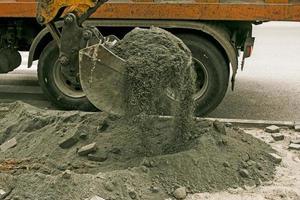 obras viales en la calle de la ciudad. el cucharón de la excavadora recoge el pavimento viejo y lo carga en un camión volquete foto