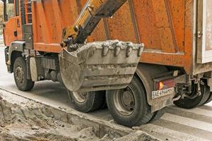 Road works on the city street. The excavator bucket collects the old pavement and loads it into a dump truck. photo