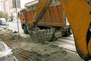 Road works on the city street. The excavator bucket collects the old pavement and loads it into a dump truck. photo