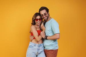 Beautiful young couple in eyeglasses embracing while standing against yellow background photo