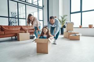 feliz familia joven sonriendo y desempacando sus cosas mientras se muda a un nuevo apartamento foto