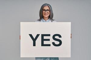 Mature beautiful female doctor looking at camera and holding placard photo