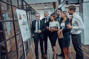 Modern businessman showing graph on the flipchart while having staff meeting in the office corridor photo