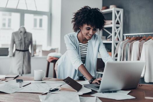 responder en el correo electrónico comercial. hermosa joven africana trabajando usando computadora y sonriendo mientras está de pie en el taller foto