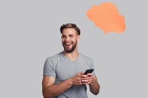 Nice message.  Handsome young smiling man holding smart phone and looking away while standing against grey background photo