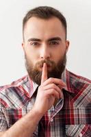Keep silence. Portrait of handsome young bearded man making salience sign photo