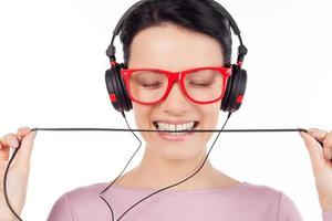 It is her favorite song. Beautiful young woman in red glasses and headphones listening to the music and keeping eyes closed while isolated on white photo