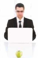 Only fresh ideas. Confident young man in formalwear working on computer while sitting at his working place with green apple laying on foreground photo