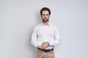 Handsome young man in white shirt looking at camera while standing against gray background photo