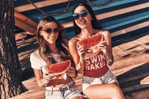 Juicy and sweet. Top view of two attractive young women smiling and eating watermelon while sitting outdoors photo