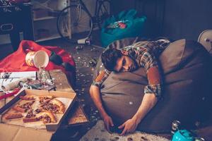 lugar cómodo para desmayarse. joven apuesto se desmayó en una bolsa de frijoles con joystick en la mano en una habitación desordenada después de la fiesta foto