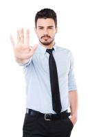 Stop it Confident young man in shirt and tie showing his palm and looking at camera while standing against white background photo