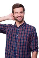 Cheerful handsome. Portrait of handsome young man in casual shirt holding hand behind head and smiling while standing isolated on white photo