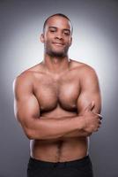 Proud of his fit body. Young shirtless African man looking at camera and smiling while keeping arms crossed and standing against grey background photo