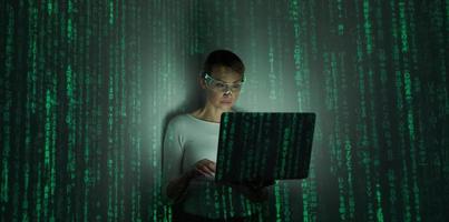 Confident woman in futuristic glasses using computer against background with green symbols photo