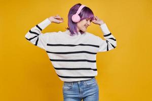 Joyful young woman with headphones dancing against yellow background photo