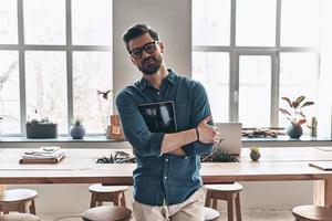 Confident business expert. Handsome young man holding digital tablet and looking at camera with smile while standing in the office photo