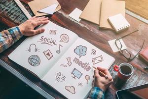 Social media. Top view close-up image of man holding hands on his notebook with colorful sketches while sitting at the wooden desk photo