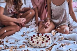 se ve delicioso. cerca de cuatro mujeres jóvenes en pijama preparándose para comer pastel mientras tienen una fiesta de pijamas foto