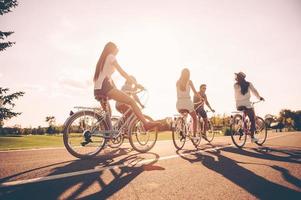 Enjoying beautiful day together. Low angle view of young people riding bicycles along a road and looking happy photo