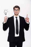 Good idea Excited young man in formalwear pointing up and holding picture of electric lamp while standing against white background photo