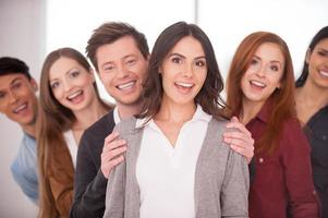 She is real leader. Attractive young woman smiling while group of cheerful young people standing behind her in two rows photo