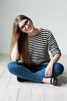 Cute and flirty. Beautiful young woman in striped clothing sitting on the hardwood floor and holding hand on chin photo