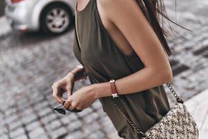 Always in style. Close-up of young woman holding her eyewear while walking outdoors photo