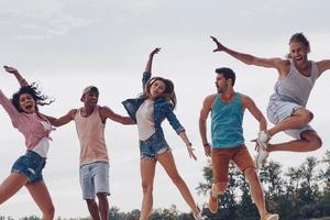 Summer fun. Full length of young people in casual wear smiling and gesturing while jumping on the pier photo