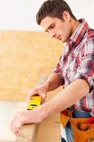 Everything should be perfect. Confident young handyman working with wood in workshop photo