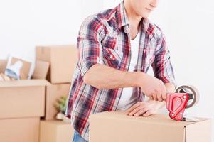 Preparing to moving. Close-up of man packing boxes while other cardboard boxes laying in the background photo