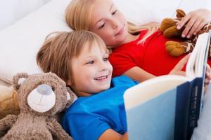 leyendo su libro favorito. dos lindos niños leyendo un libro juntos mientras están acostados en la cama juntos foto