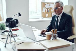Senior man in elegant business suit using modern technologies while making social media video photo