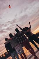 High in the sky. Rear view of young people embracing and gesturing while looking at floating sky lantern photo