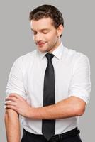 Ready to work. Confident young man in shirt and tie adjusting his sleeves while standing against grey background photo