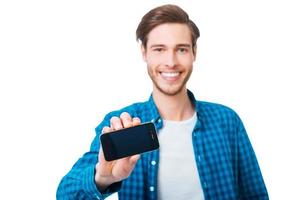 This smart phone can be yours. Happy young man stretching out mobile phone and smiling while standing against white background photo